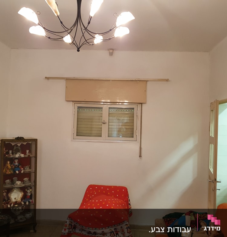 חדר עם קירות לבנים, מנורה תלויה ותמונות על מדף